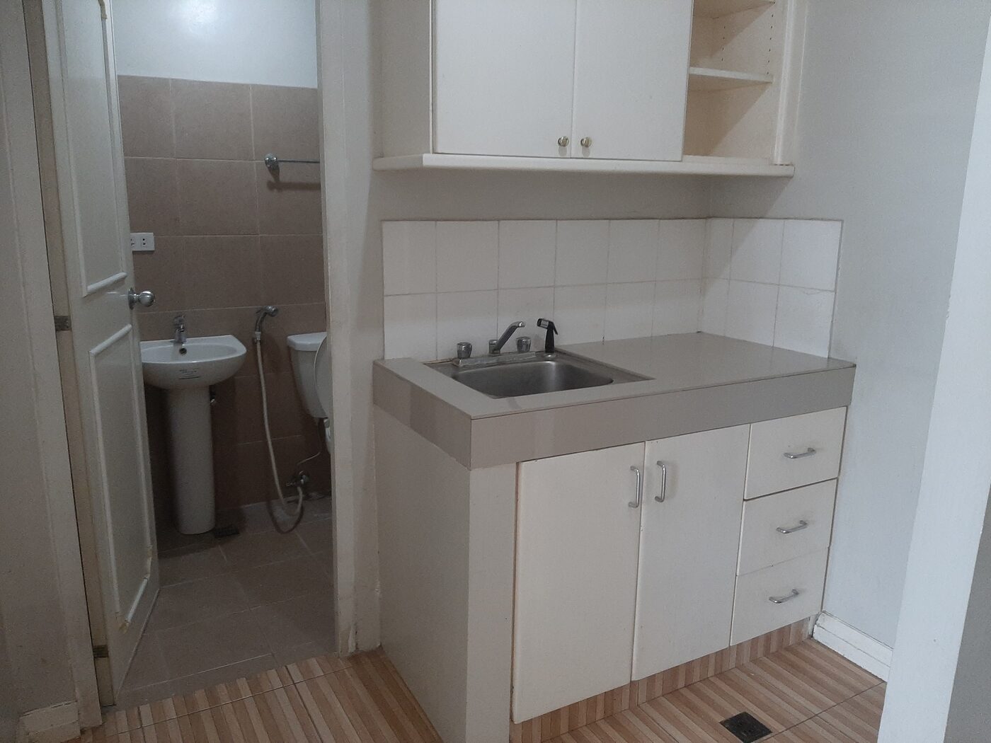 Kitchenette with sink, counter and cabinets beside the bathroom door in the Palm Towers Makati studio