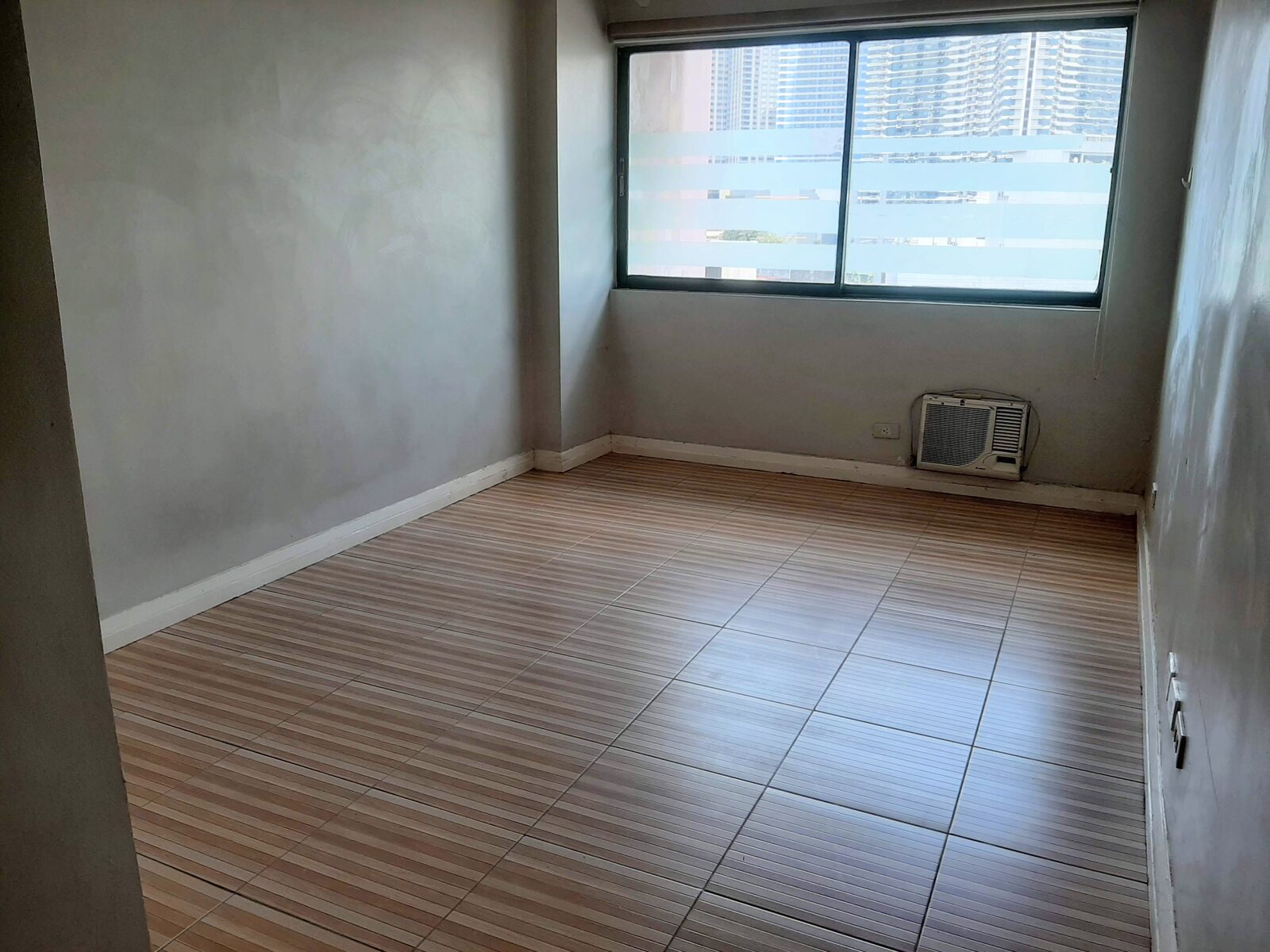 28 sqm studio unit interior at Palm Towers, San Antonio Village, Makati, with wood-look tile flooring, wide window and window-type aircon